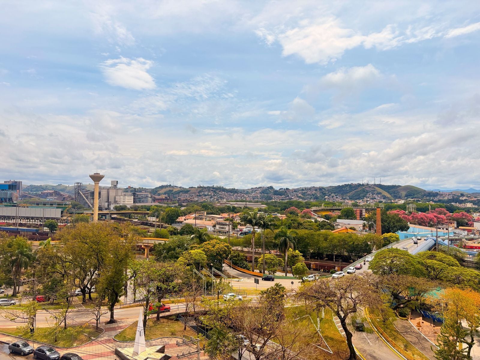 Un paisaje urbano con una torre destacada, un puente y un parque con árboles.
