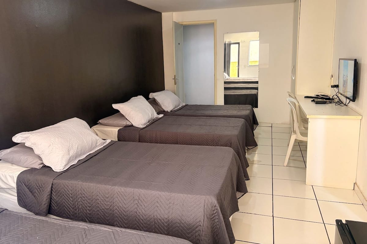 Hotellihuone, jossa on kolme sänkyä, työpöytä, televisio ja ovi, joka johtaa toiseen huoneeseen.