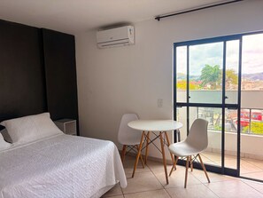 Quarto com cama, uma mesinha, duas cadeiras, varanda com vista e ar condicionado.