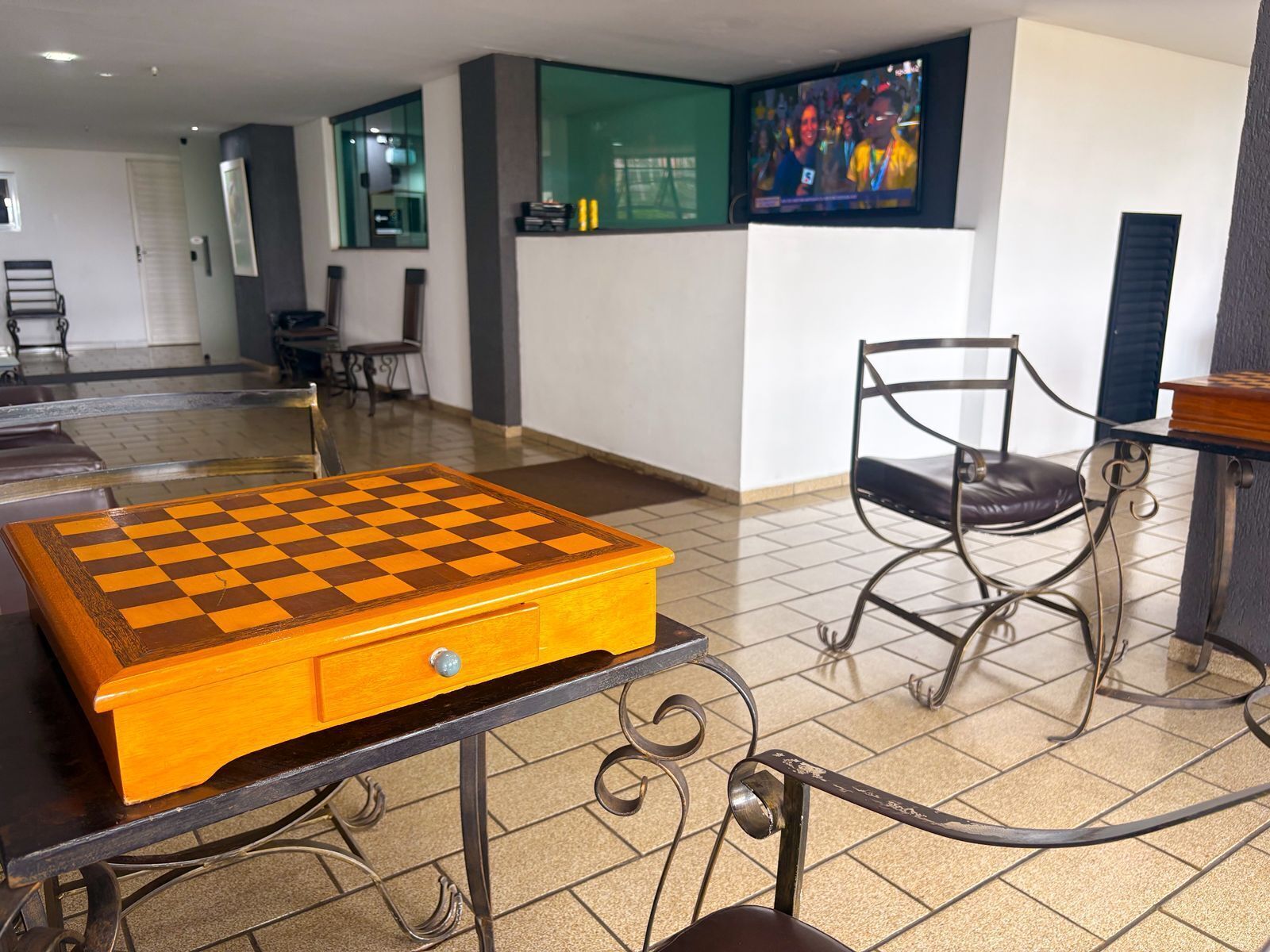 Una mesa de ajedrez con cajón, una silla metálica y un televisor fijado a la pared.