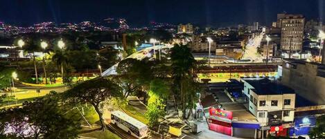 Un paisaje urbano nocturno con una estación de autobuses, una estatua y un edificio con un letrero rojo.