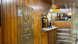 A hotel reception area with wooden paneling, a reception desk, a staircase, and a sign indicating the hotel's name and location. - Stratus Centro Hotel (Volta Redonda)