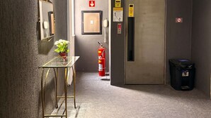 A hallway with a glass table, a mirror, a fire extinguisher, and a door. - Stratus Centro Hotel (Volta Redonda)