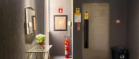 Un pasillo con una mesa de vidrio, un espejo, un extintor y una puerta.