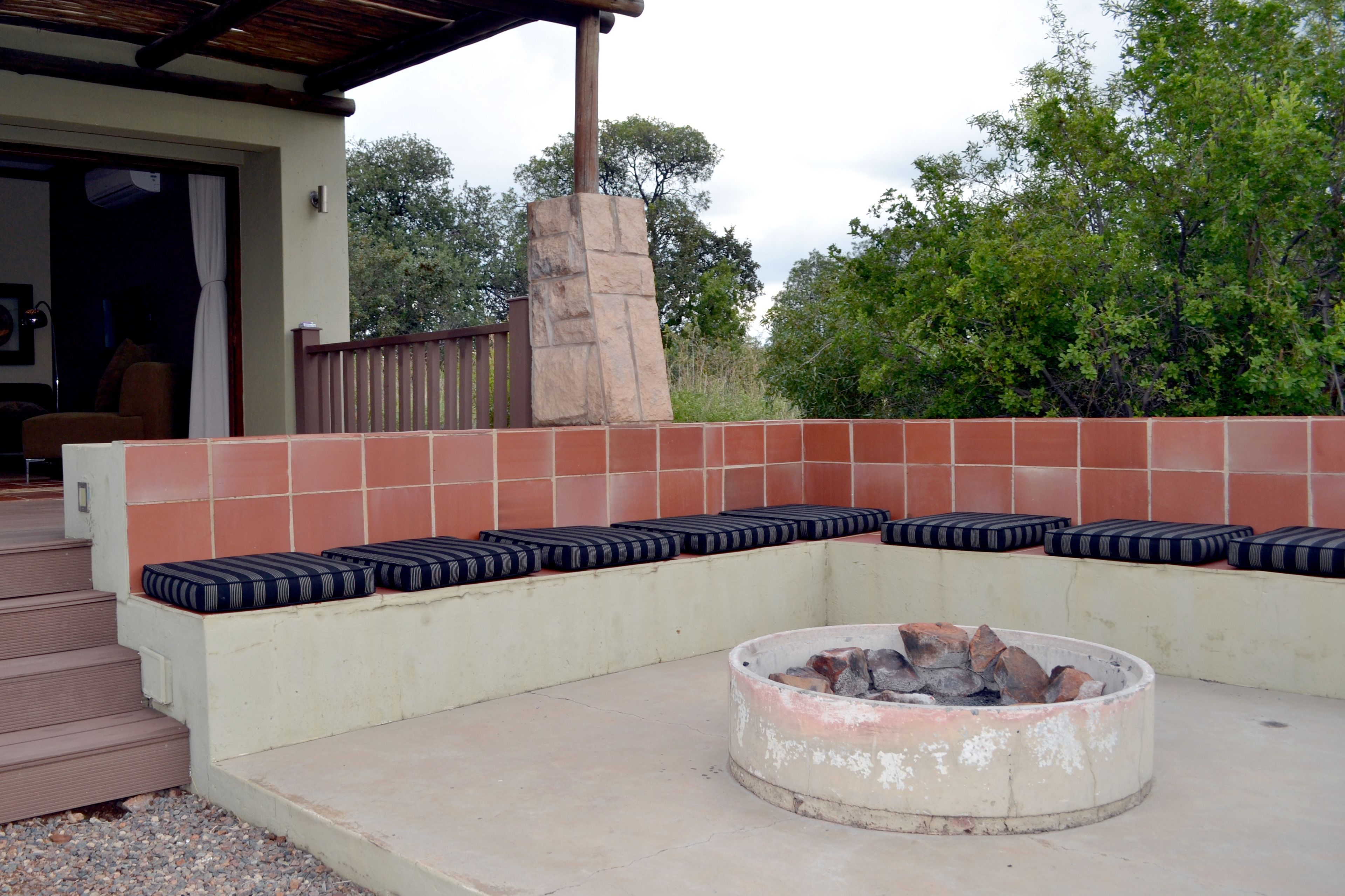 A covered outdoor seating area with a fire pit, steps leading to a door, and a stone pillar.