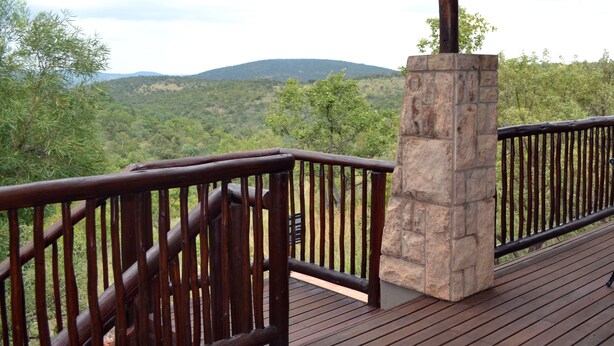 Una terraza de madera con un pilar de piedra y vistas a un paisaje montañoso.