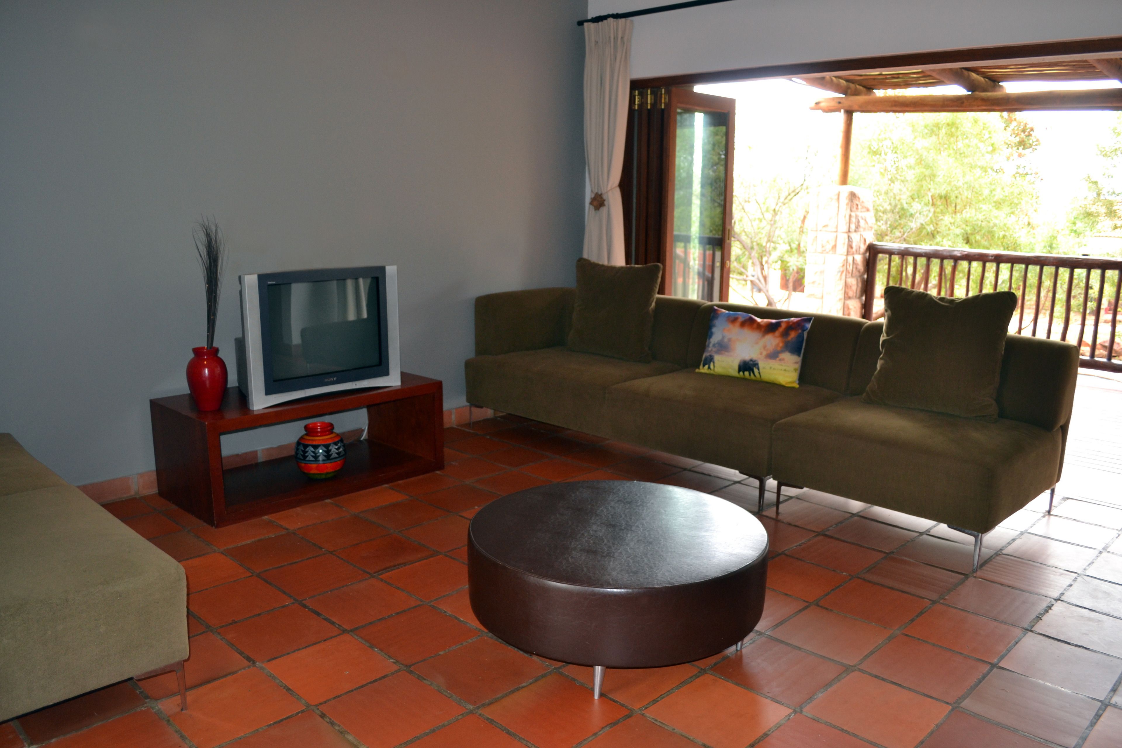 A living room with a sofa, a television on a wooden stand, a round coffee table, and a window with curtains.