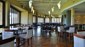 Un comedor espacioso con techos altos, varias mesas y sillas, y grandes ventanales que dejan entrar luz natural.