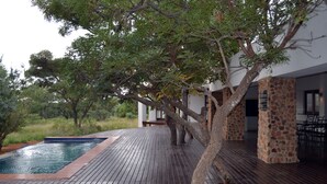 Una terraza de madera con piscina, rodeada de árboles y un edificio de piedra.