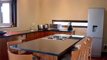 Cocina compacta con una isla central, sillas de madera, horno integrado, refrigerador y ventana que proporciona luz natural.