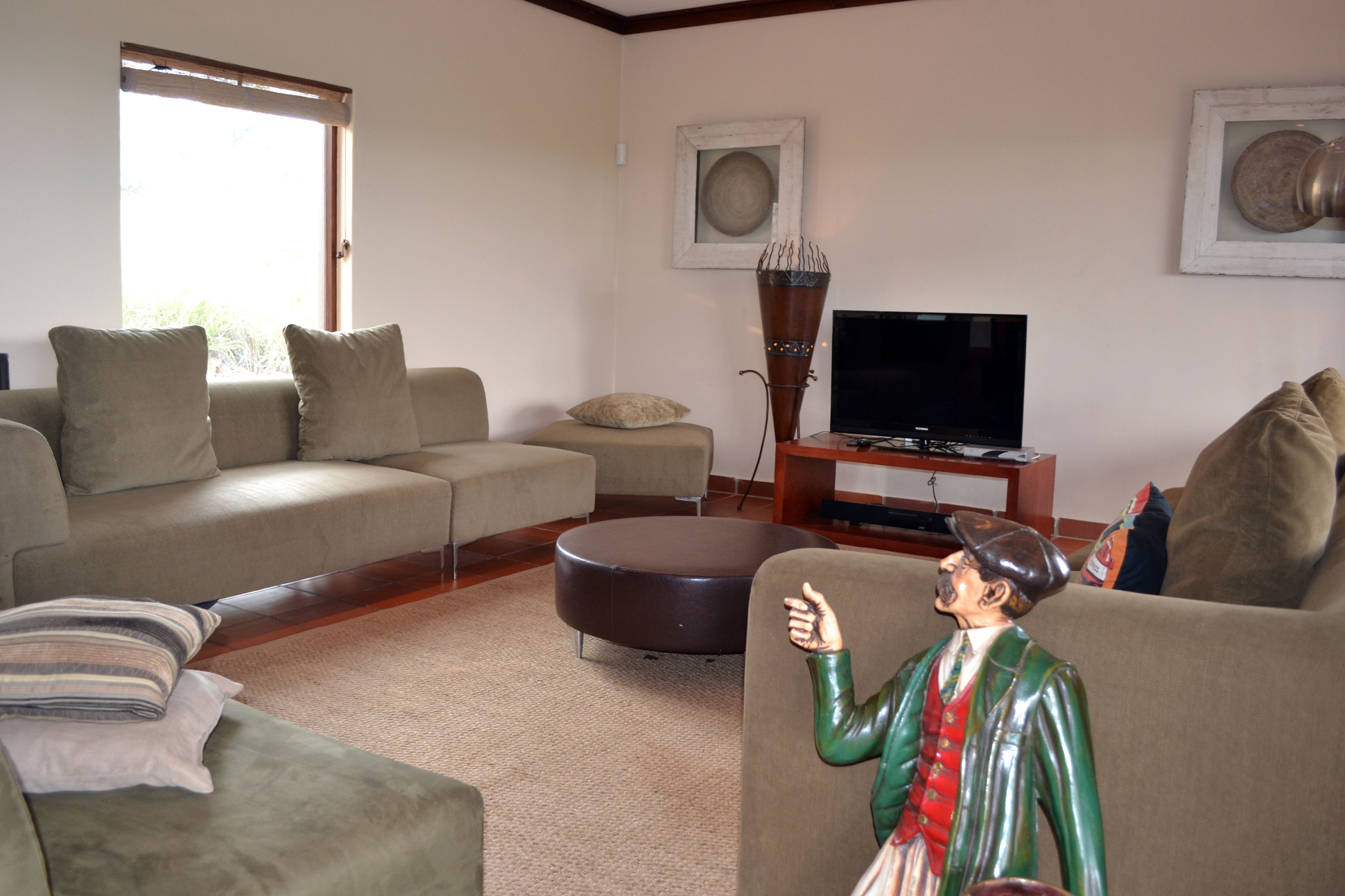 A living room with a sofa, ottoman, and a statue. There is a television and a framed picture on the wall.