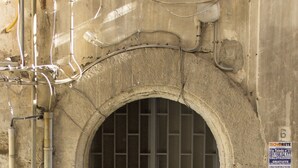 An arched doorway with a metal grille, a sign with text, and exposed pipes. - Sui Tetti di Napoli (Naples)