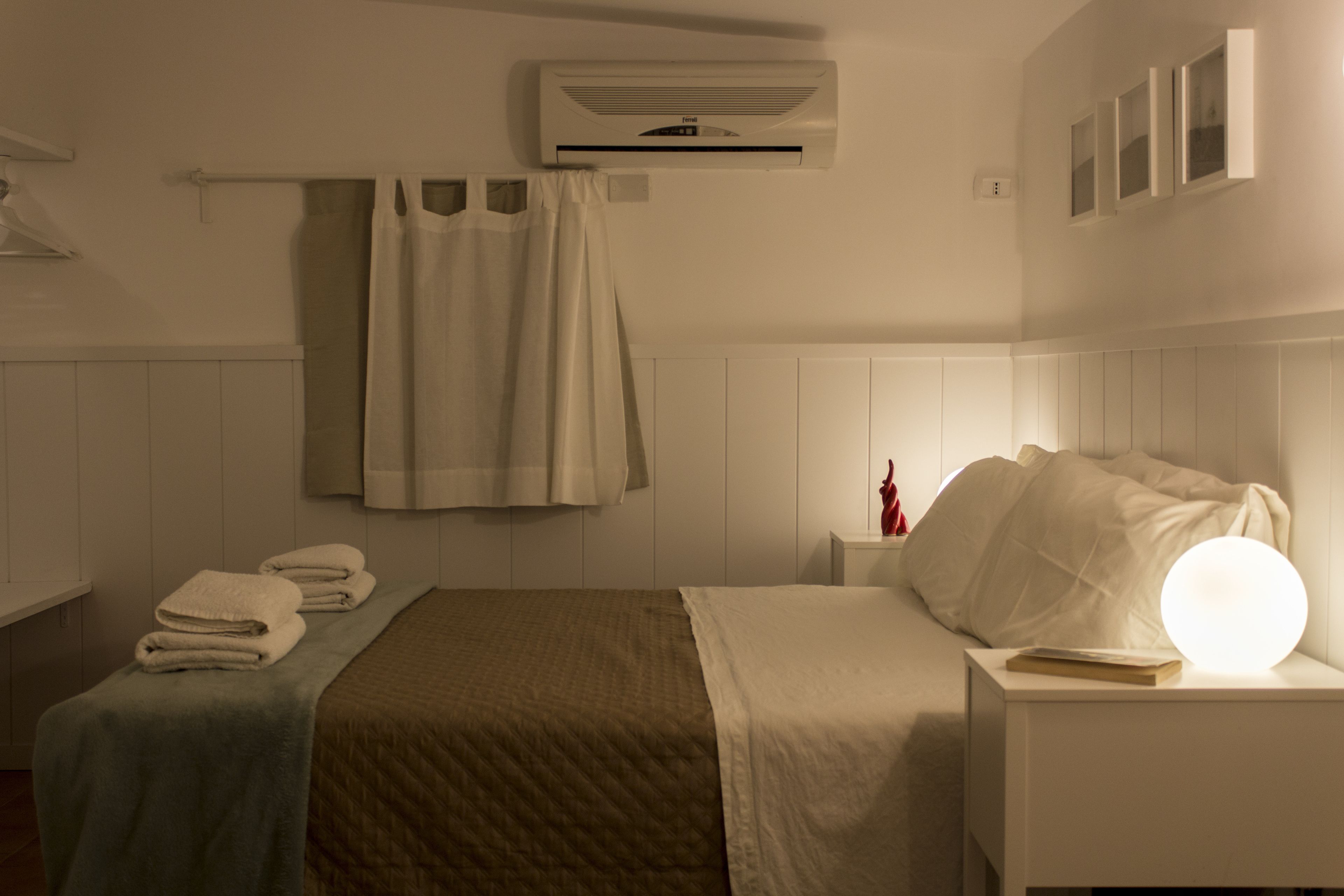 Une chambre d’hôtel comprenant un lit, une table de chevet avec une lampe, un porte-serviettes et un appareil de climatisation.