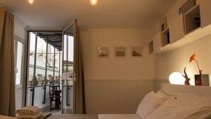 A hotel room with a bed, a window with curtains, a view of the outside, and a shelf with decorative items. - Sui Tetti di Napoli (Naples)