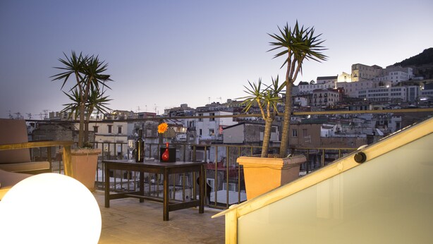 A rooftop terrace with potted plants, a table with a vase, and a railing. - Sui Tetti di Napoli (Naples)