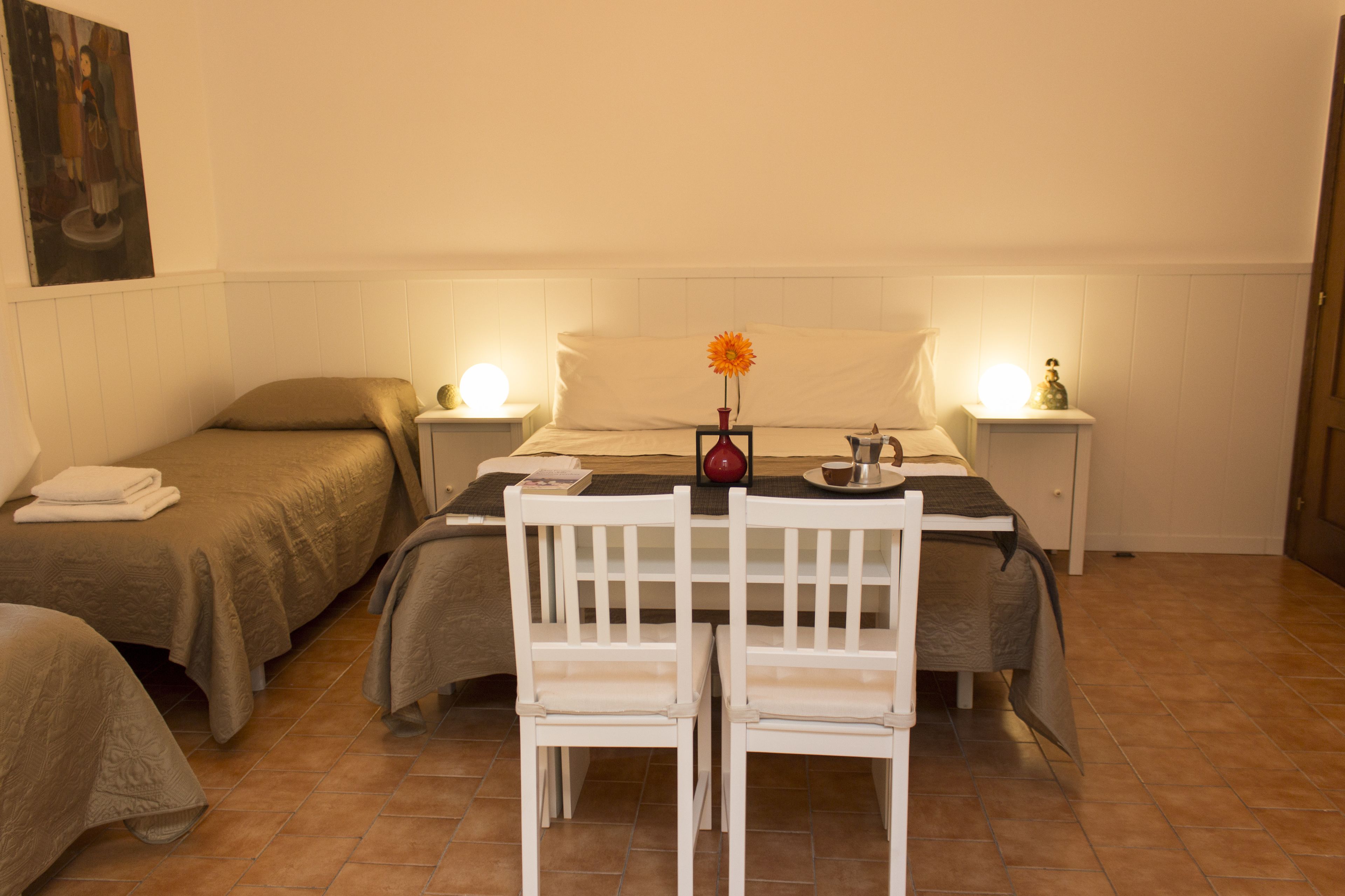 A bedroom with two beds, a small table with chairs, and bedside lamps.