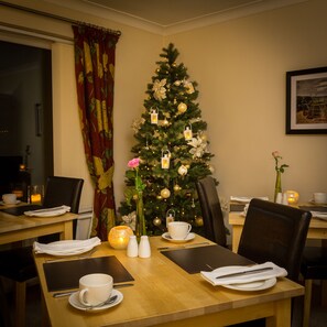 A dining area with a Christmas tree, a vase with a pink rose, salt and pepper shakers, and a candle on the table. - Hermiston Guest House (Keswick)