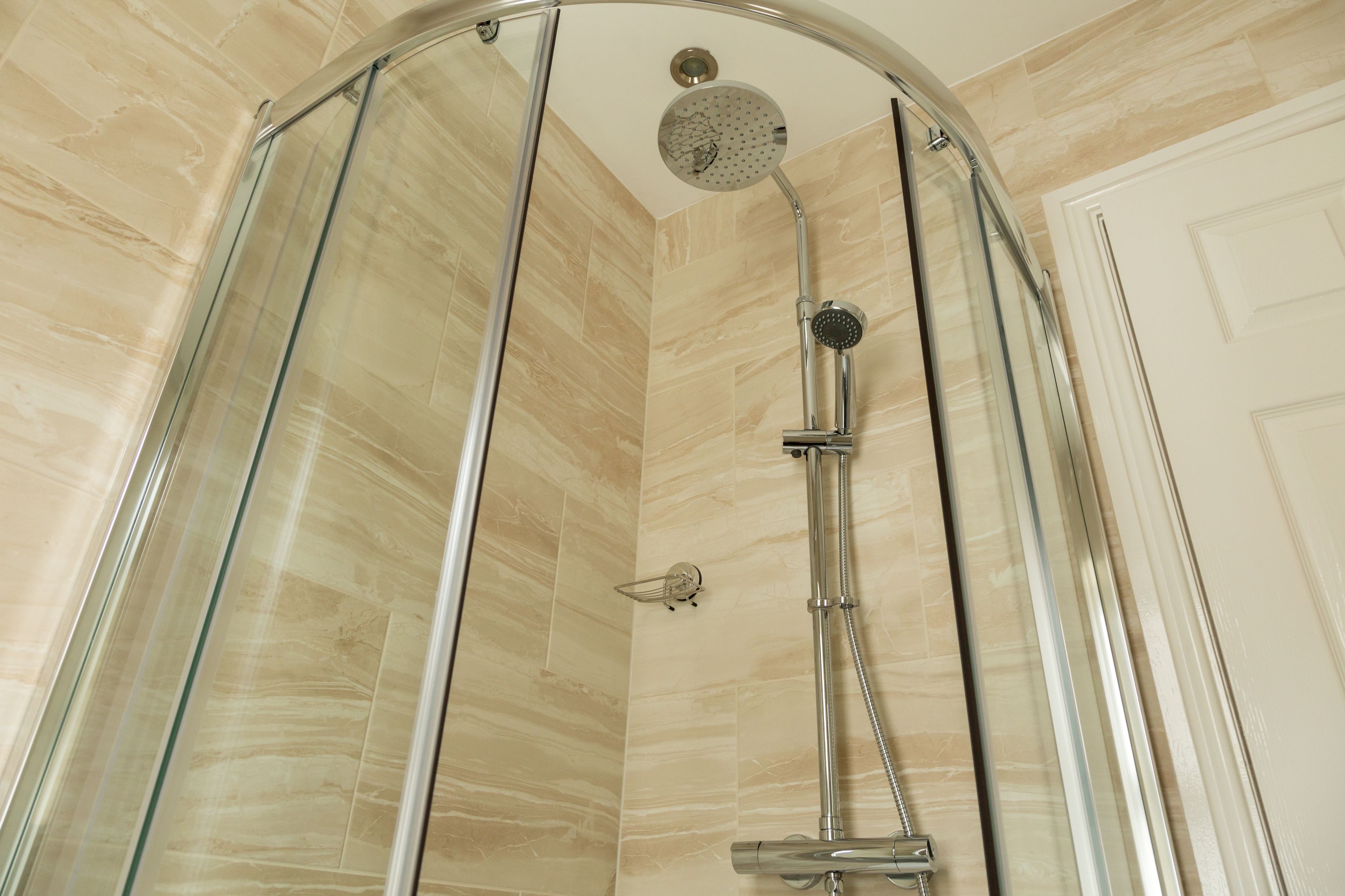 A glass-enclosed shower with a handheld showerhead and a wall-mounted faucet.