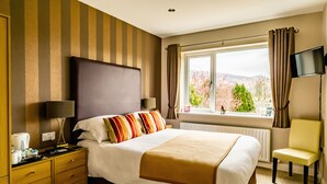 A hotel room with a large bed, a bedside table with lamps, a chair, a TV, and a window with curtains. - Hermiston Guest House (Keswick)