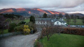 A rural landscape with a house surrounded by greenery, a paved driveway, and a road with vehicles. - Hermiston Guest House (Keswick)