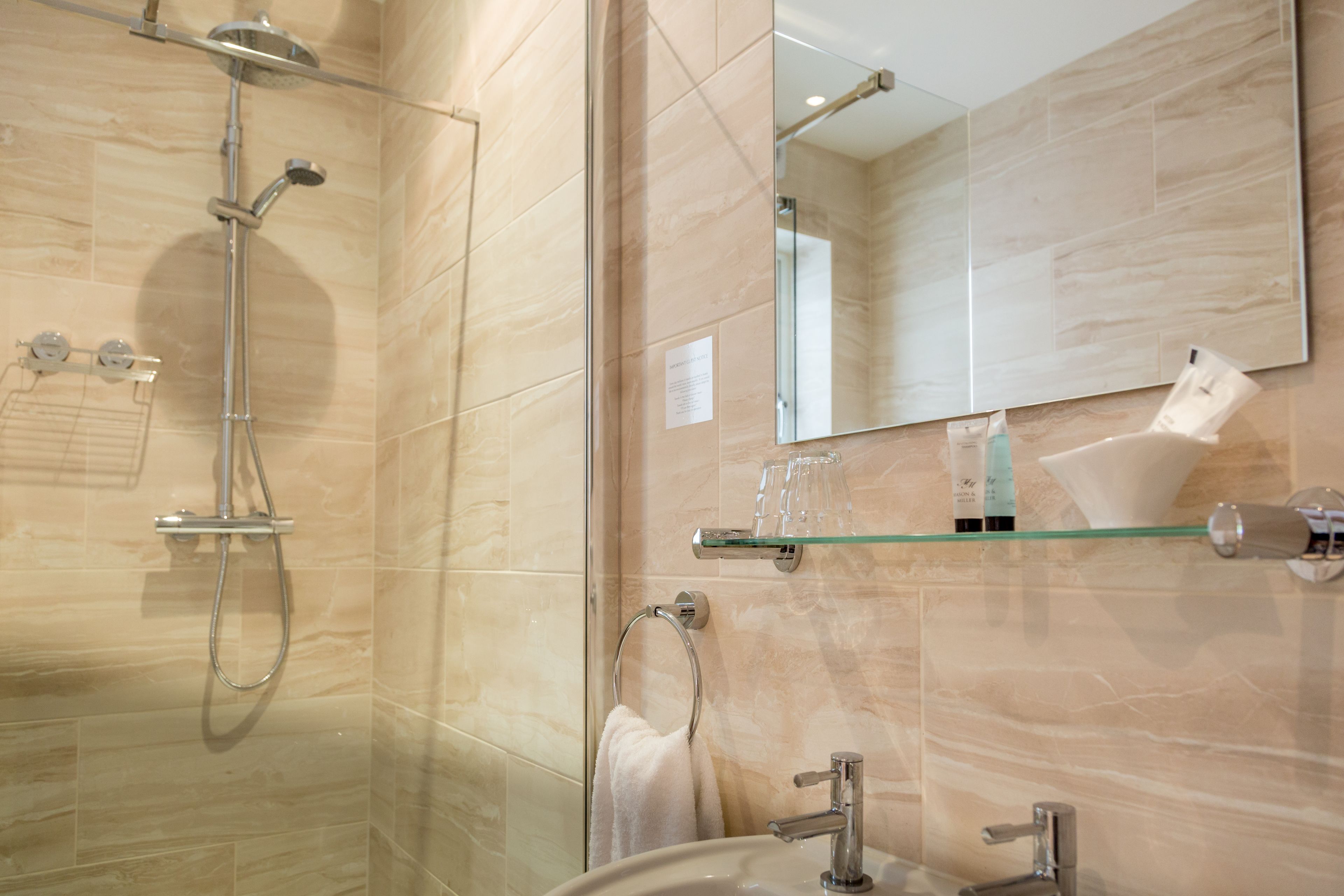 Een moderne badkamer met een douchecabine van glas, een wastafel met spiegel en een glazen plank met toiletartikelen.