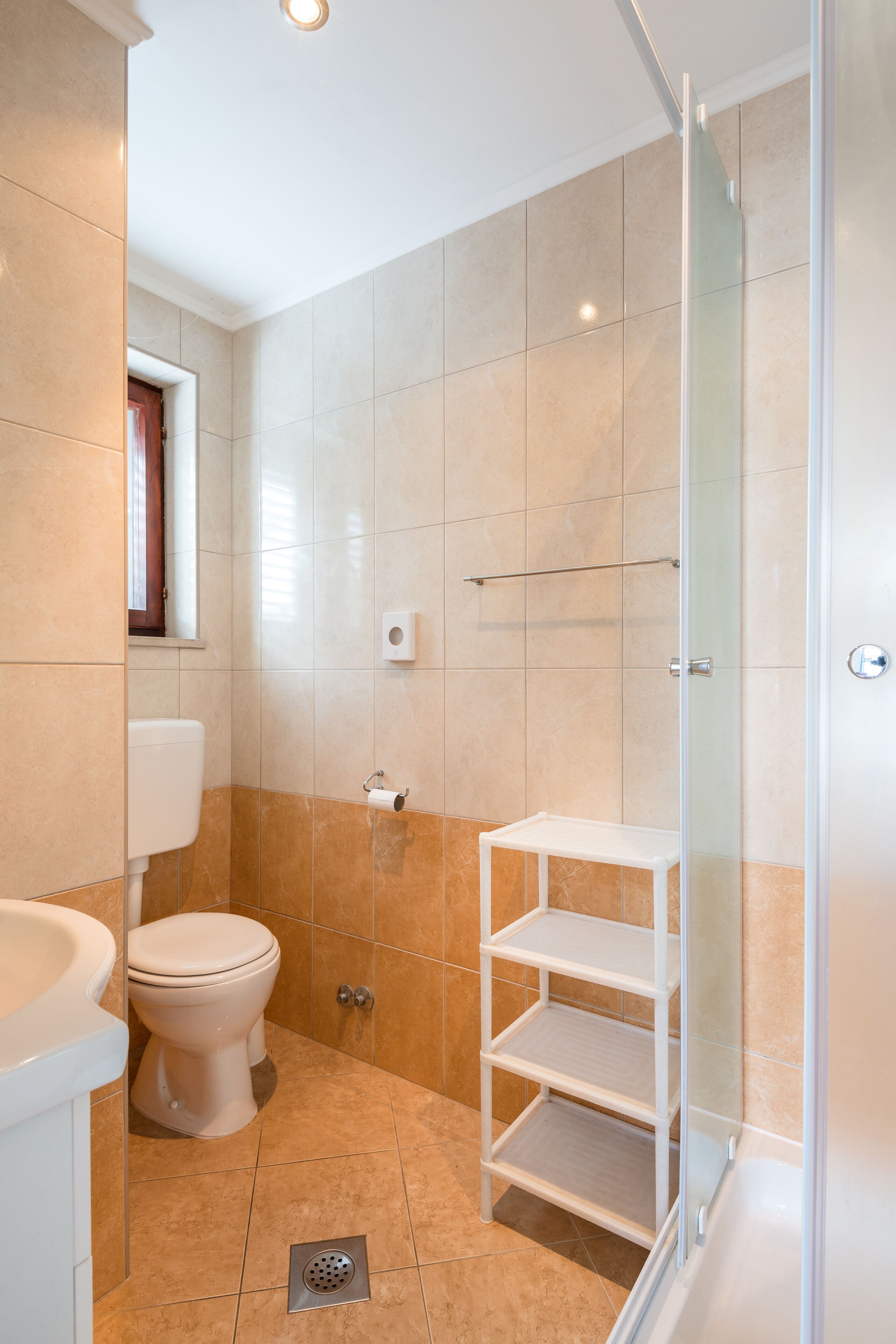Et badeværelse med toilet, håndvask, brusebad og en brusekabine med glasvægge.