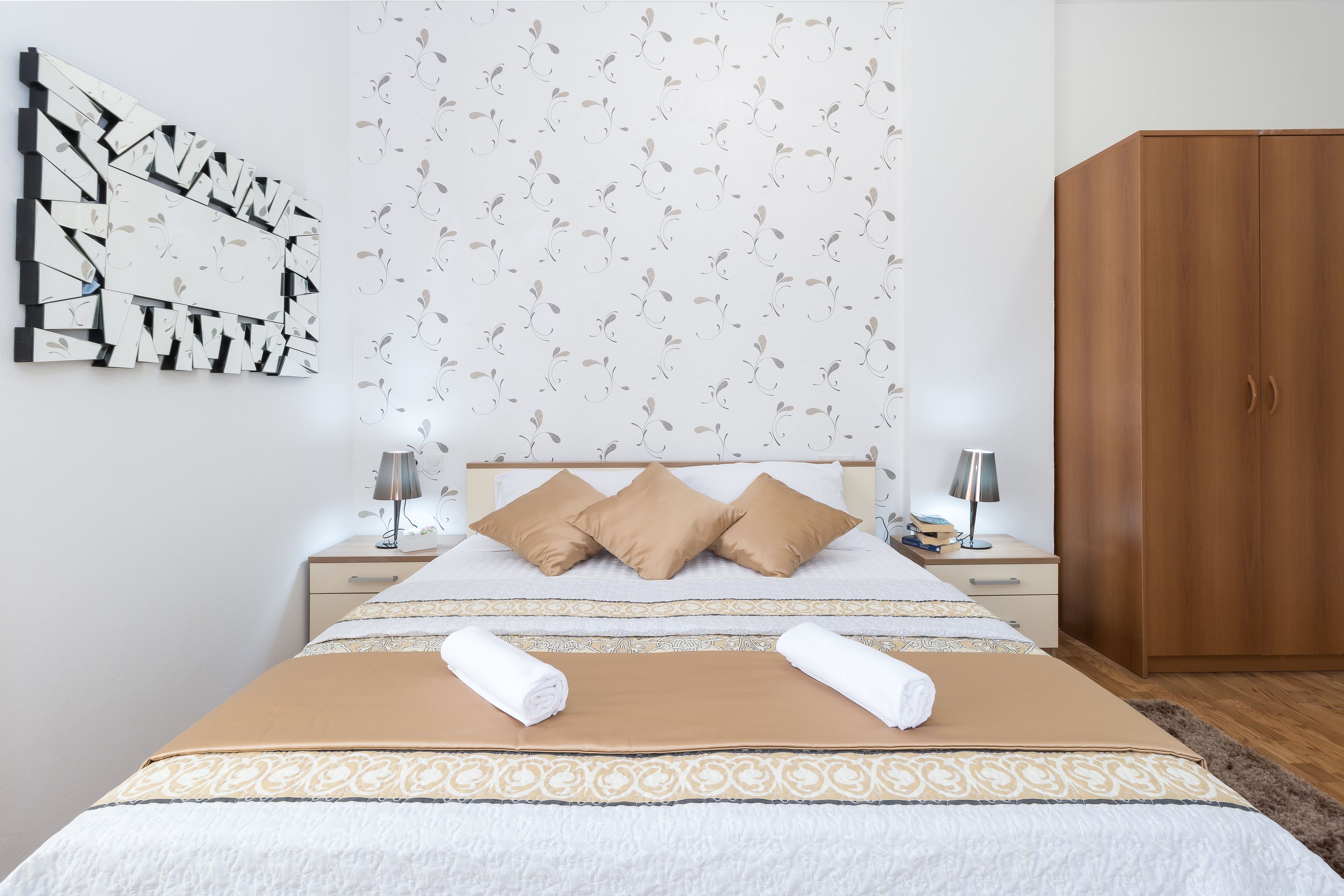Ein ordentlich eingerichtetes Hotelzimmer mit einem Bett, zwei Nachttischen, einem Kleiderschrank und einem an der Wand befestigten, abstrakten Kunstwerk.