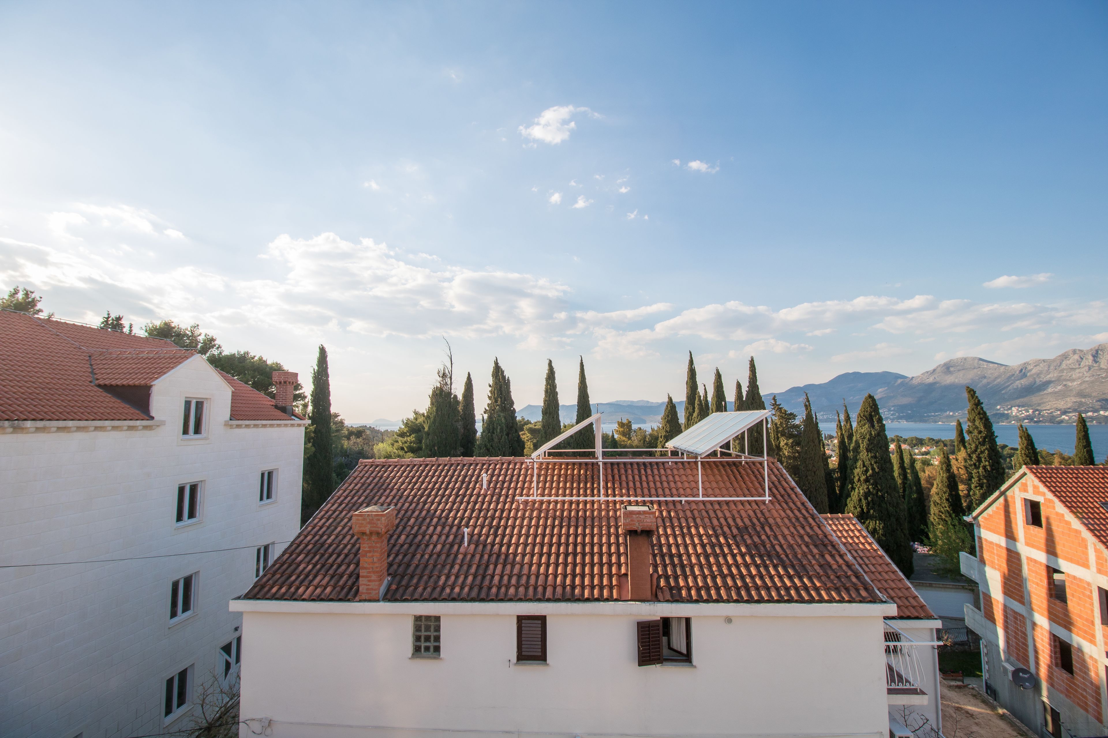 Un edificio residencial con techo de tejas rojas, varias ventanas y vistas a un lago y montañas al fondo.