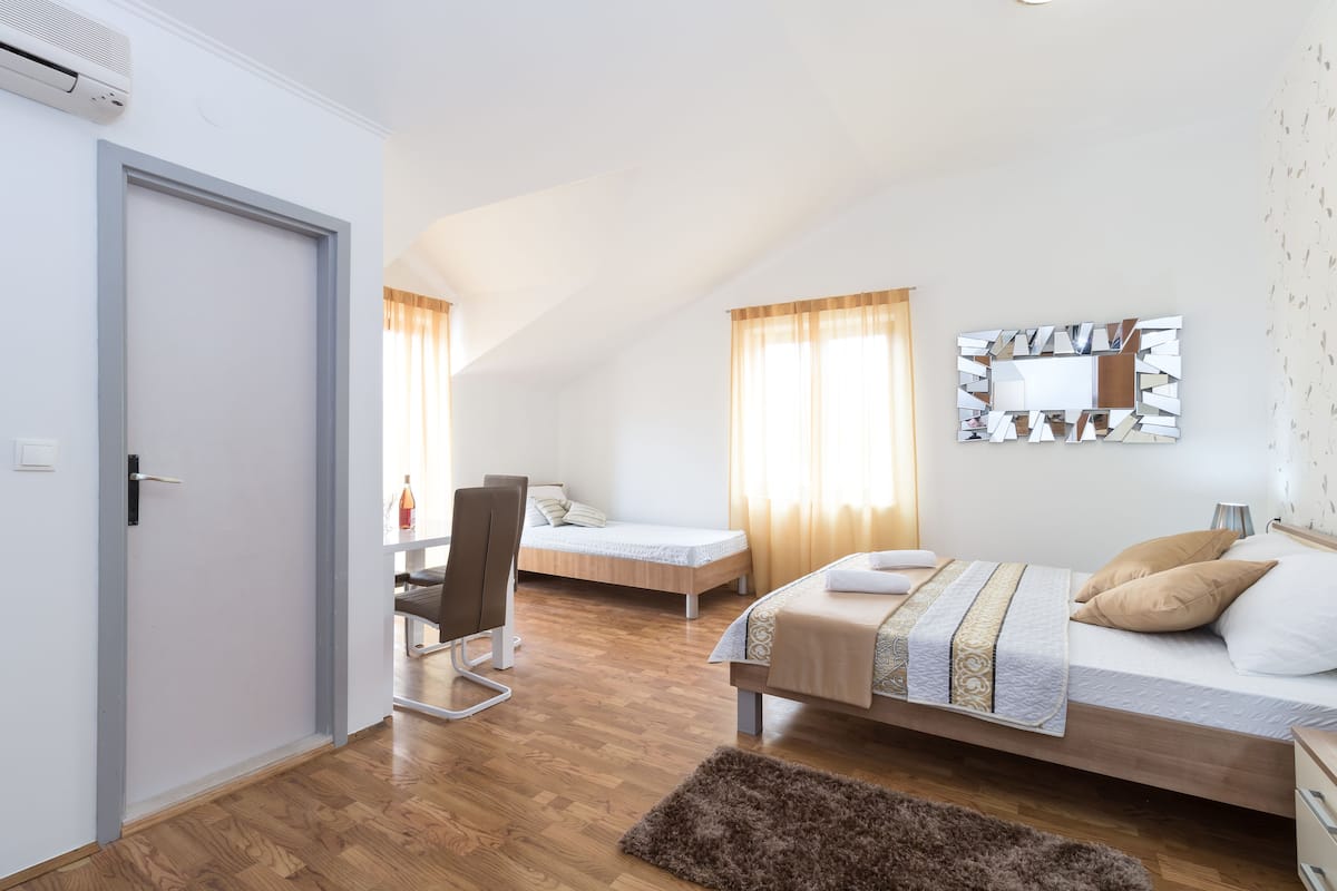 Une chambre avec un lit, un bureau et une chaise. Il y a une fenêtre avec des rideaux, un miroir sur le mur et une porte.