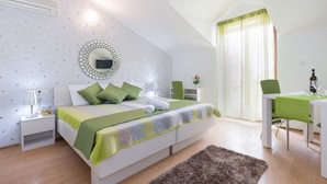 A bedroom with a bed, bedside tables, a mirror, a green chair, and a dining table with a green tablecloth. - Villa Voinić (Konavle)