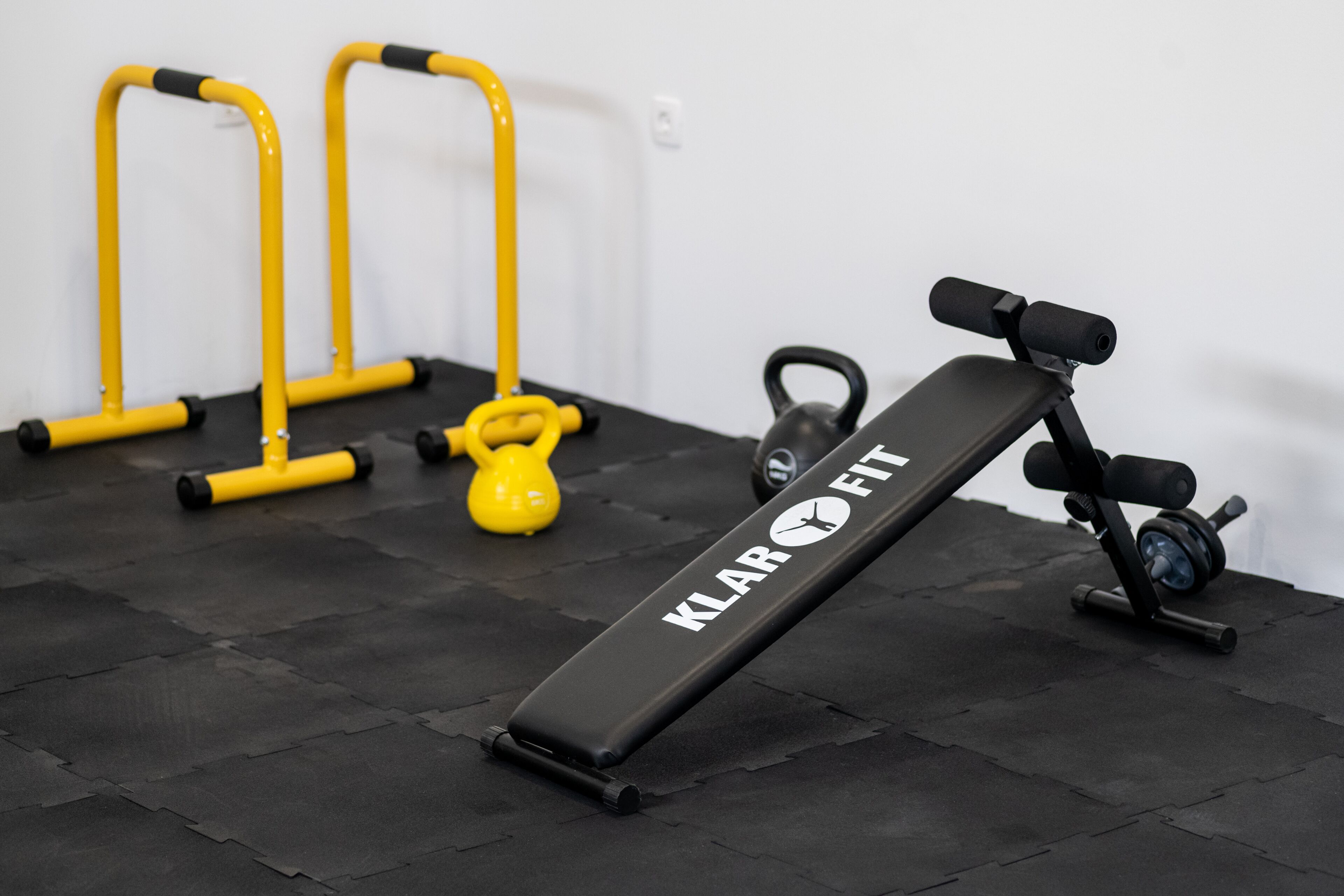 Zona de equipamiento de gimnasio con una banca, mancuernas de fundición y bandas de resistencia amarillas.