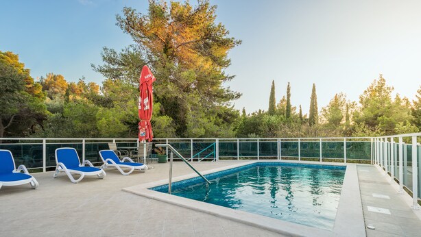 A swimming pool with blue lounge chairs and a red umbrella. - Villa Voinić (Konavle)