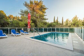 A swimming pool with blue lounge chairs and a red umbrella. - Villa Voinić (Konavle)