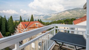 A balcony with a table and chairs, overlooking a mountainous landscape with a lake and buildings. - Villa Voinić (Konavle)