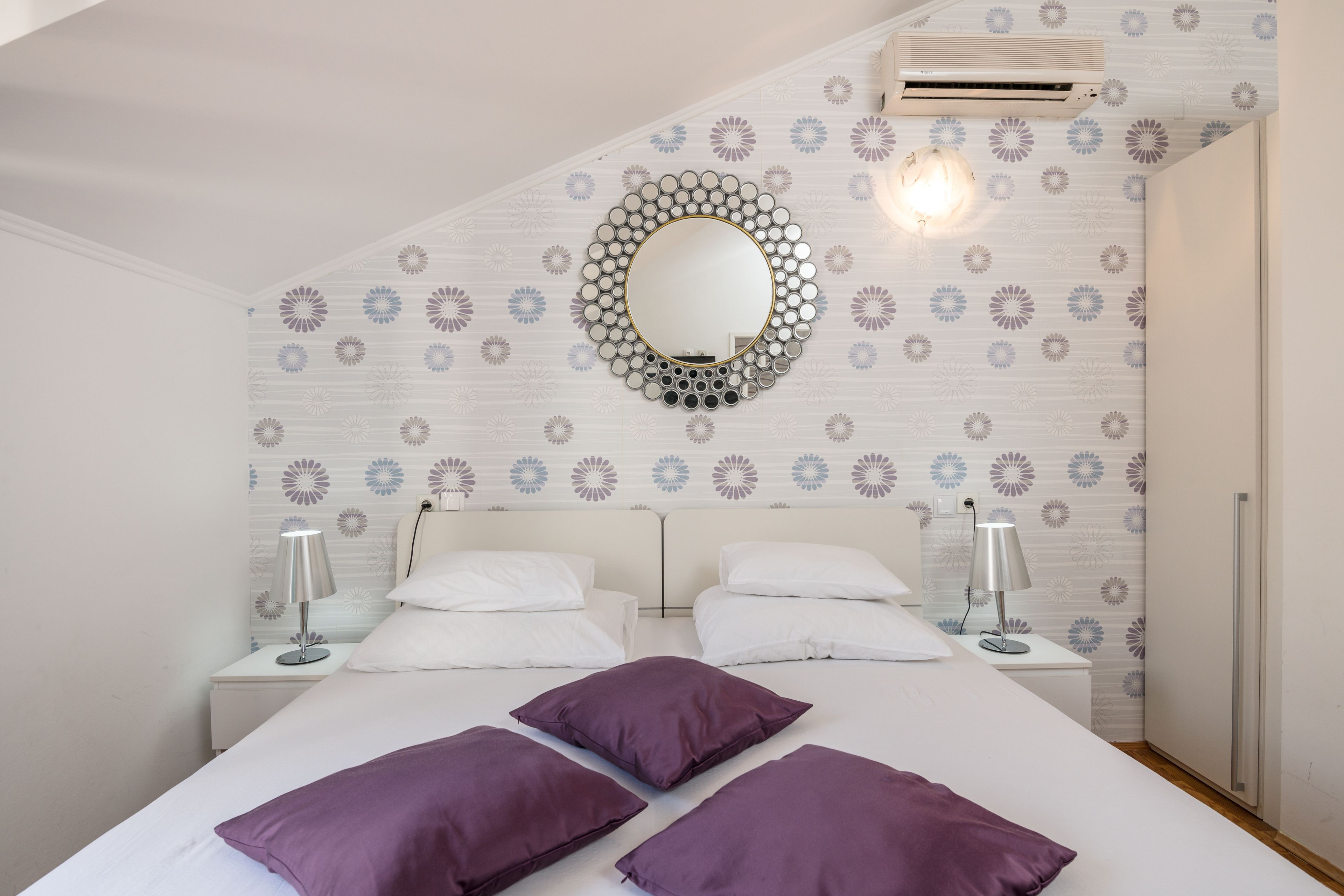 Un dormitorio con una cama, dos mesitas de noche, un espejo en la pared y un papel tapiz estampado.