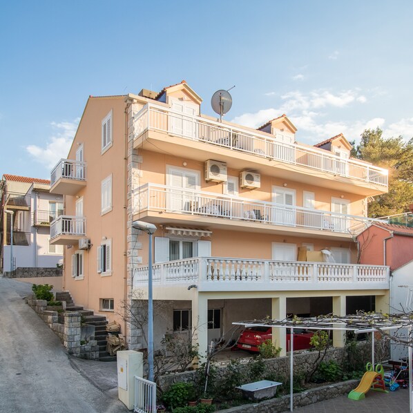 A multi-story residential building with balconies, a satellite dish, and a garage with a red car parked inside. - Villa Voinić (Konavle)