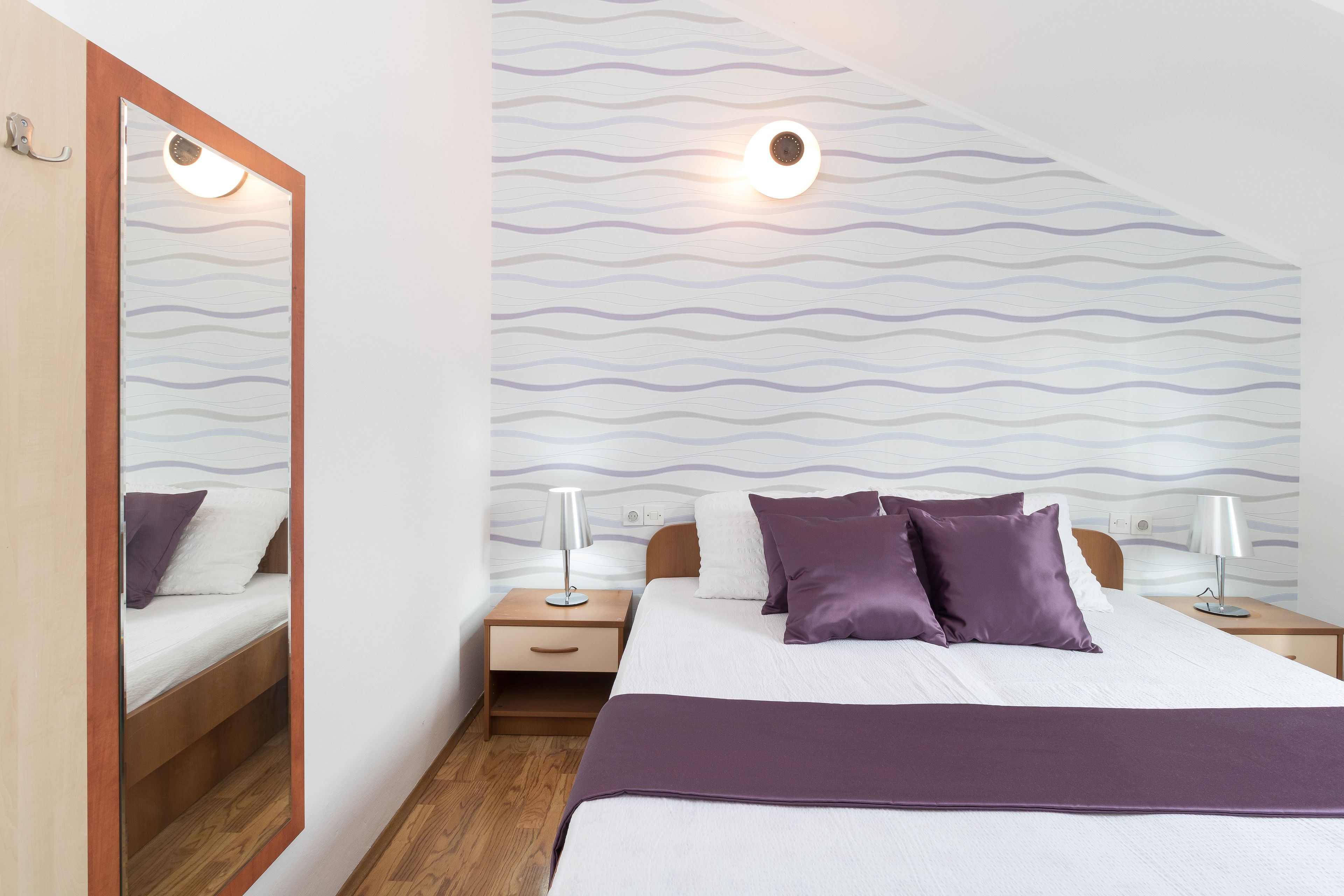 A bedroom with a bed, two bedside tables, a mirror, and a patterned wall.