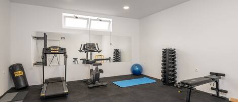 Palestra con tapis roulant, ellittica, pesi e un tappetino blu.