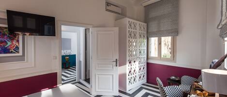 Una habitación de hotel con una cama, un televisor, una zona de comedor con una mesa y sillas, y un panel decorativo en la pared.