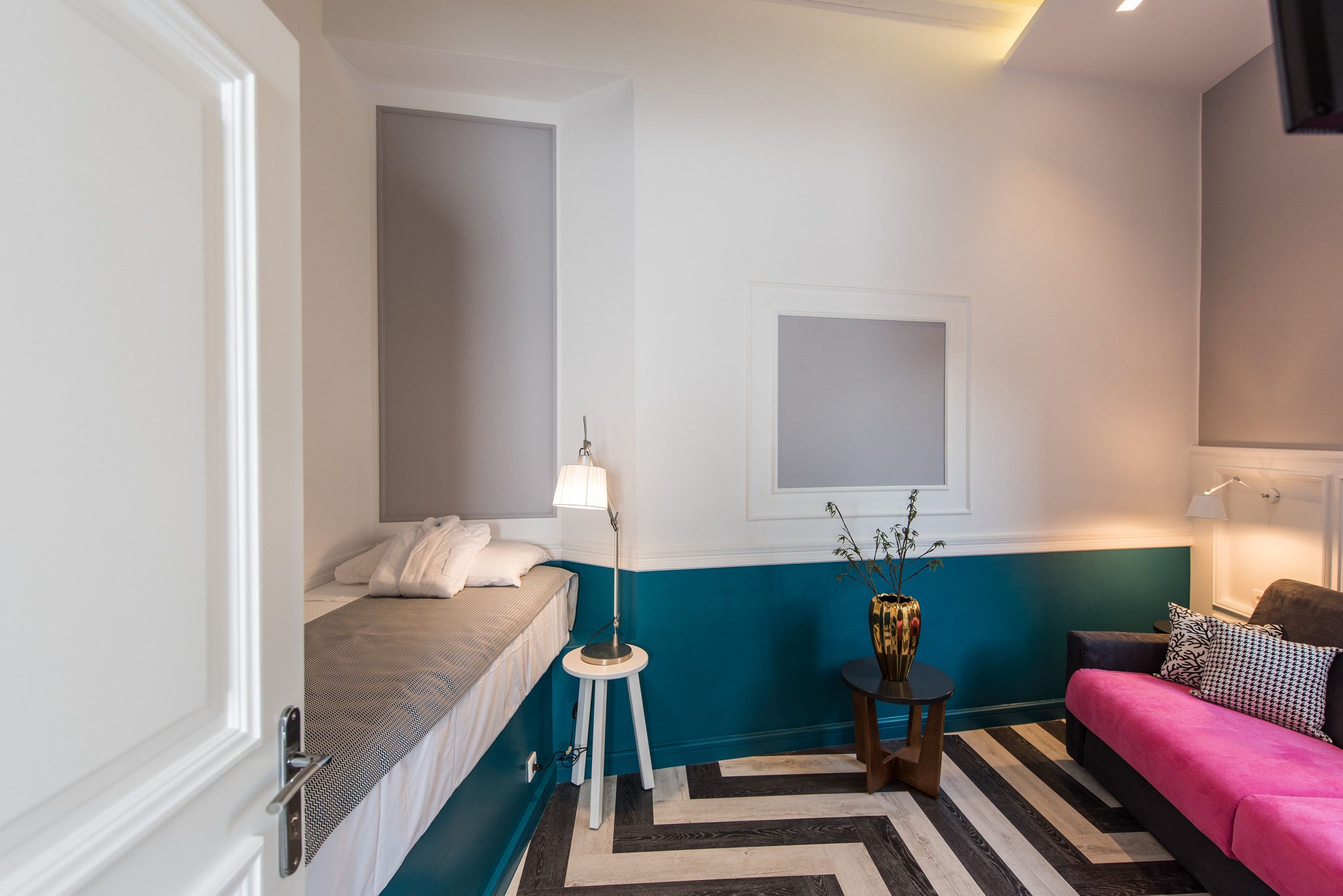A compact room with a bed, a small table with a lamp, a sofa, and a decorative vase.