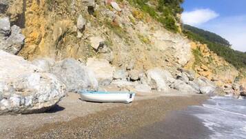 Une plage rocheuse avec un petit bateau et un gros rocher.
