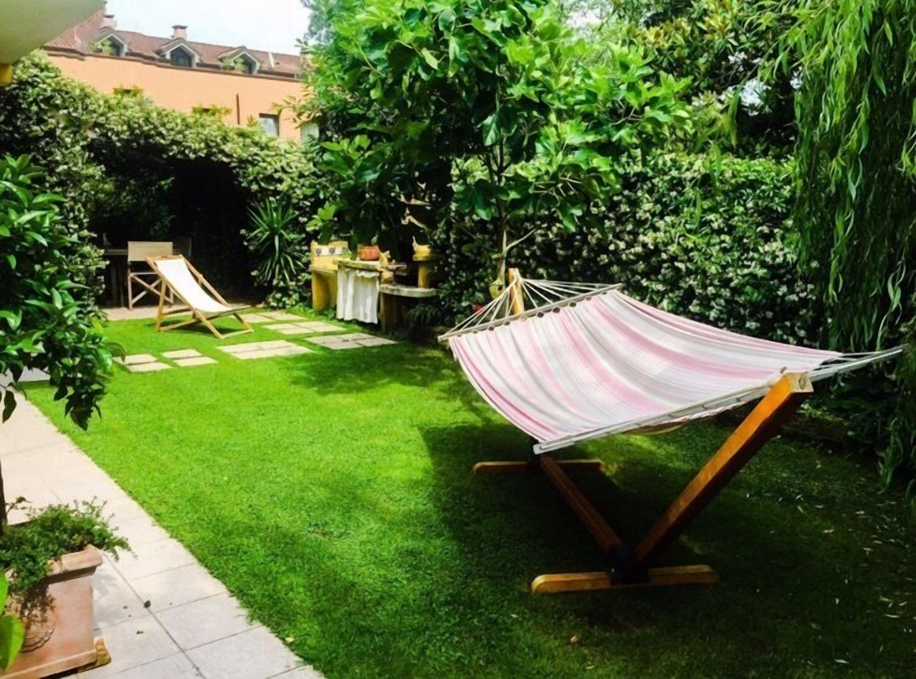 Un'amaca in un giardino curato, con prato, un tavolino e una sedia.