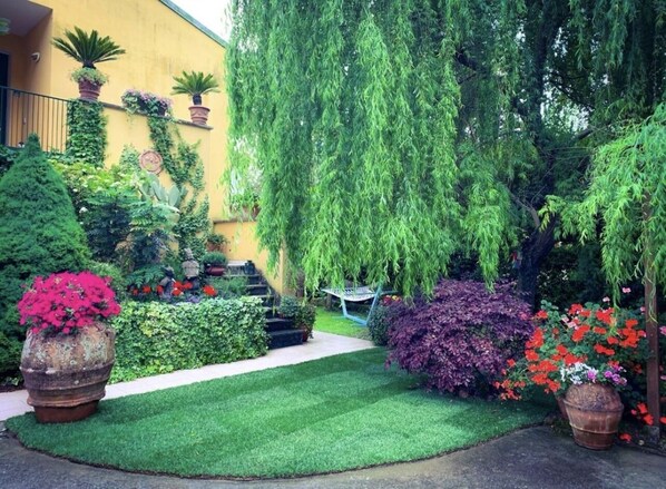 Un jardin bien entretenu, avec une variété de plantes et de fleurs, une pelouse soigneusement taillée et un chemin menant à un bâtiment.