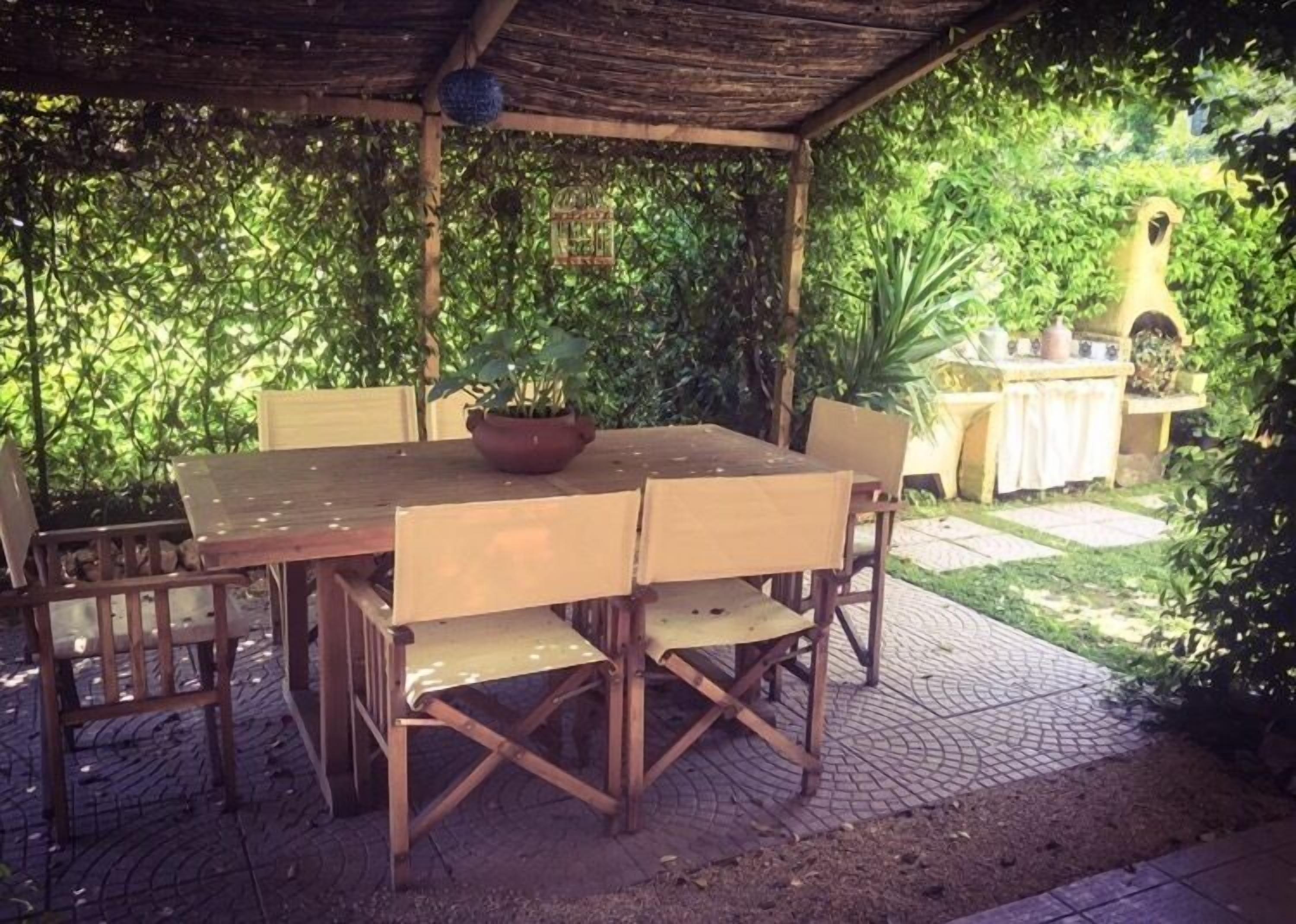 An outdoor wooden table with chairs, surrounded by lush greenery and a stone pathway.