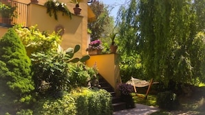 A yellow building with potted plants on the balcony, a hammock, and a weeping willow tree. - Le Pinette Bed and Breakfast (Ameglia)