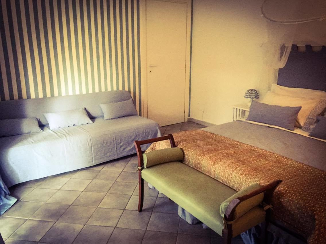 A room with a bed, a sofa, and a bench. There is a striped wall and a door in the background.