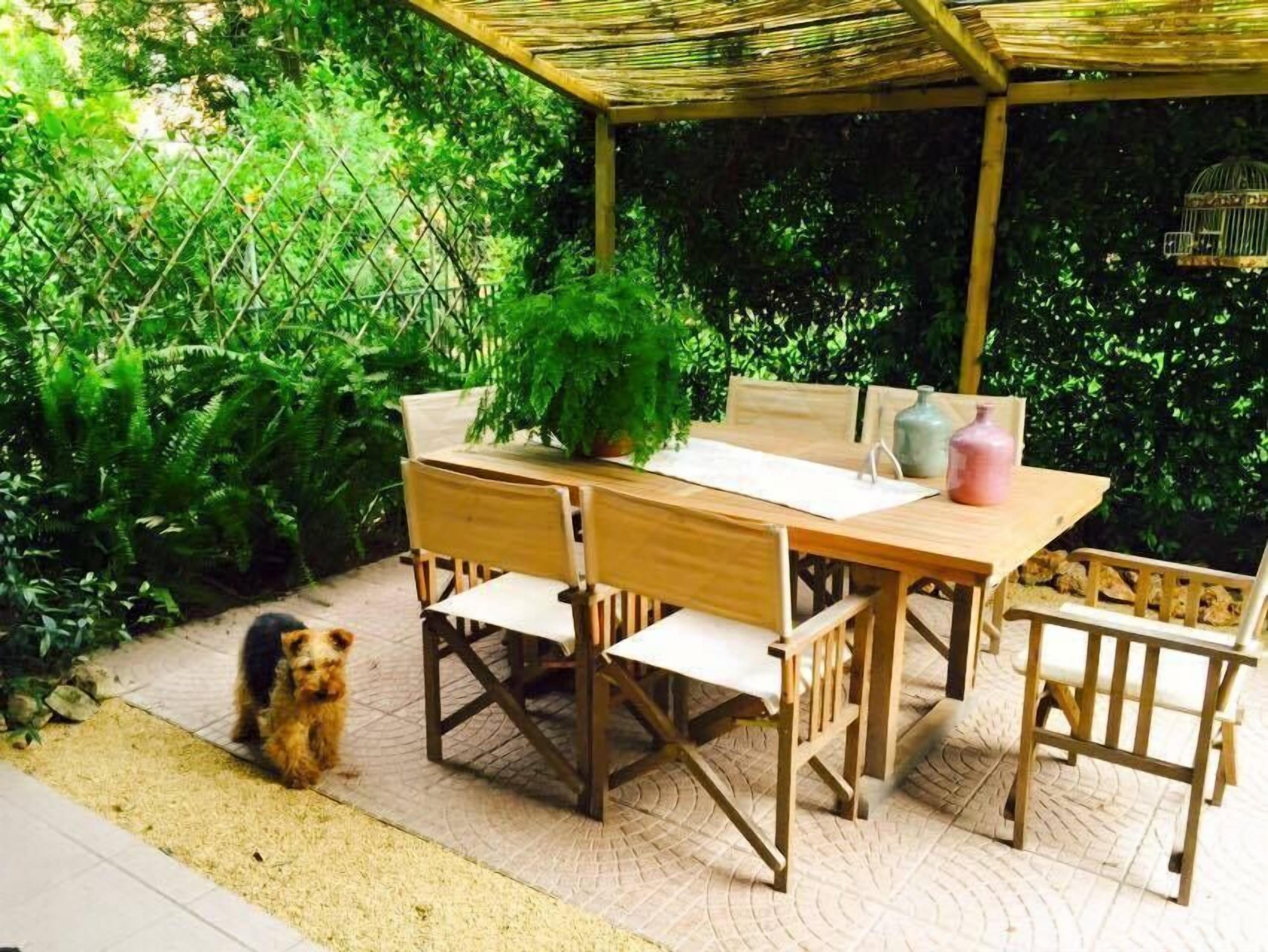 A wooden outdoor dining set with a table and chairs, a bench, and a small dog nearby.