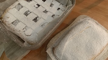 Una teglia con decorazione a reticolo, parzialmente ricoperta di farina, e un contenitore separato di farina su una superficie in legno.