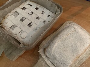 Une plaque de cuisson ornée d’un motif en croisillons, partiellement recouverte de farine, et un récipient séparé contenant de la farine, le tout posé sur une surface en bois.