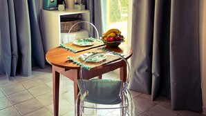 A dining area with a table set for two, a bowl of fruit, and a window with curtains. - Le Pinette Bed and Breakfast (Ameglia)